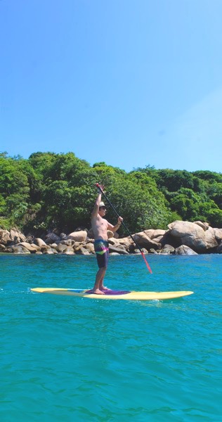 Hombre sin playera que navega en paddle board en las playas de Isla La Roqueta
