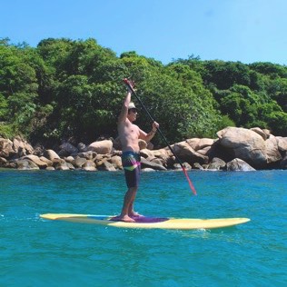 Hombre sin playera que navega en paddle board en las playas de Isla La Roqueta
